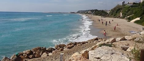 A beach with rocky terrain, a sandy shore, and a clear sky.