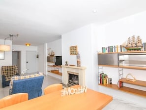 A modern living room with a fireplace, a dining area, and a bookshelf with books and decorative items. - Apartament Puig - Comarruga (Comarruga)