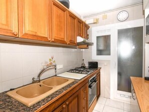 A kitchen with wooden cabinets, a double sink, a stove, and a refrigerator. - Apartament Puig - Comarruga (Comarruga)