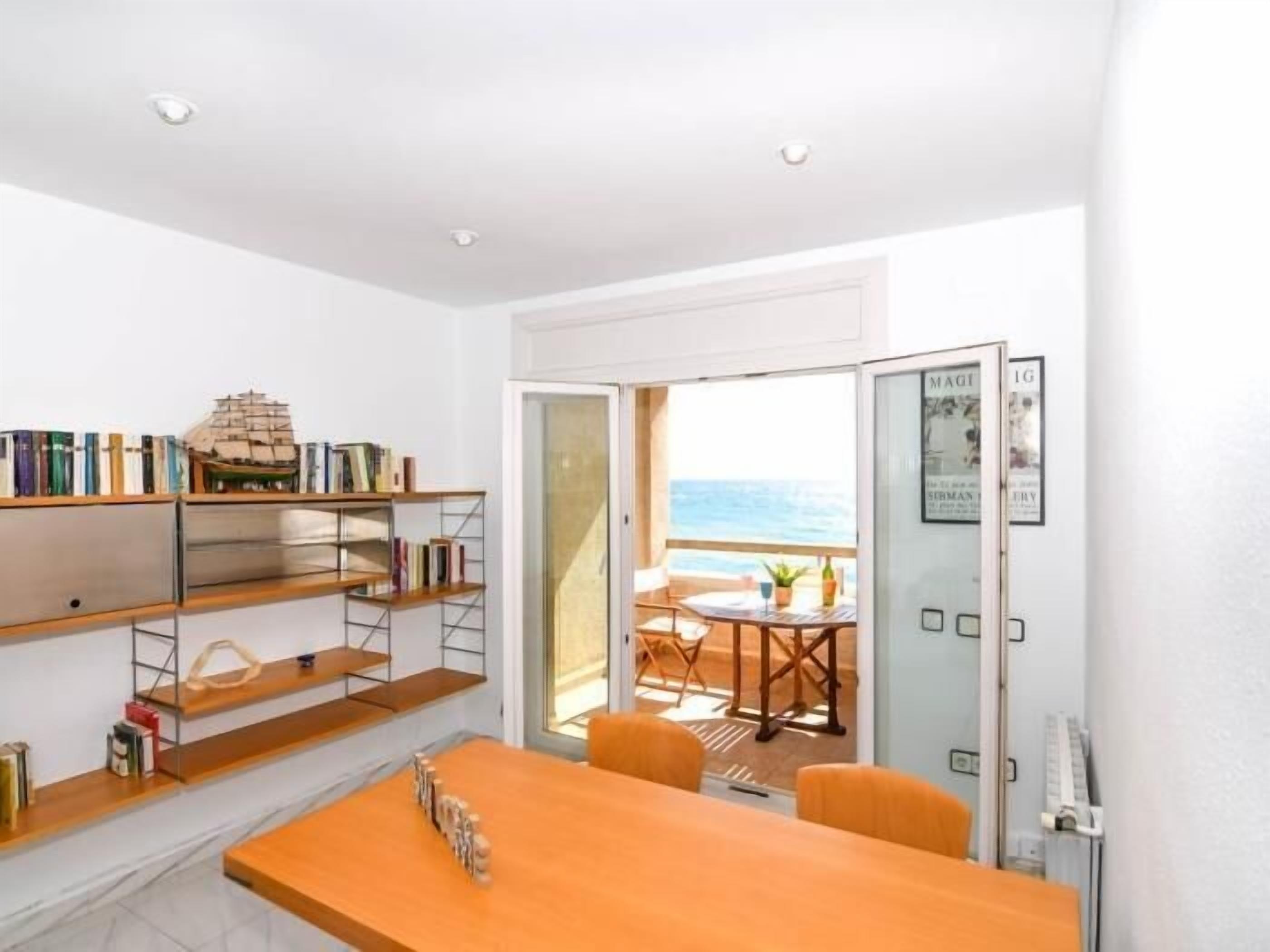 Een kamer met een houten tafel, stoelen, een boekenkast en een balkon met uitzicht.