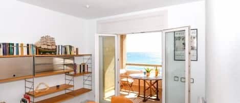A room with a wooden table, chairs, a bookshelf, and a balcony with a view.