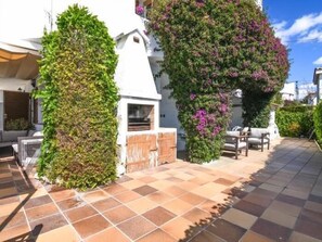A residential property with a tiled patio, a wooden fence, and a white building with a chimney. - Casa Socias - Comarruga (Comarruga)