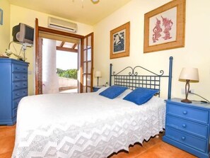 Une chambre à coucher comprenant un lit, une commode, une table de chevet et une porte donnant sur un espace extérieur.