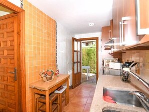 A compact kitchen with a wooden table, a sink, and a view of a garden through an open door. - Casa Socias - Comarruga (Comarruga)