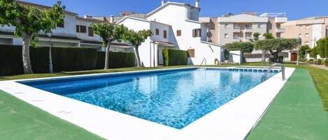 A swimming pool surrounded by a green lawn, with white buildings in the background.