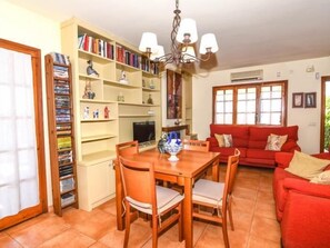 Un salon avec un canapé rouge, une table à manger en bois avec des chaises, une bibliothèque et un téléviseur.