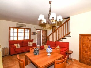 A living room with a red sofa, wooden dining table, and a staircase. - Casa Socias - Comarruga (Comarruga)