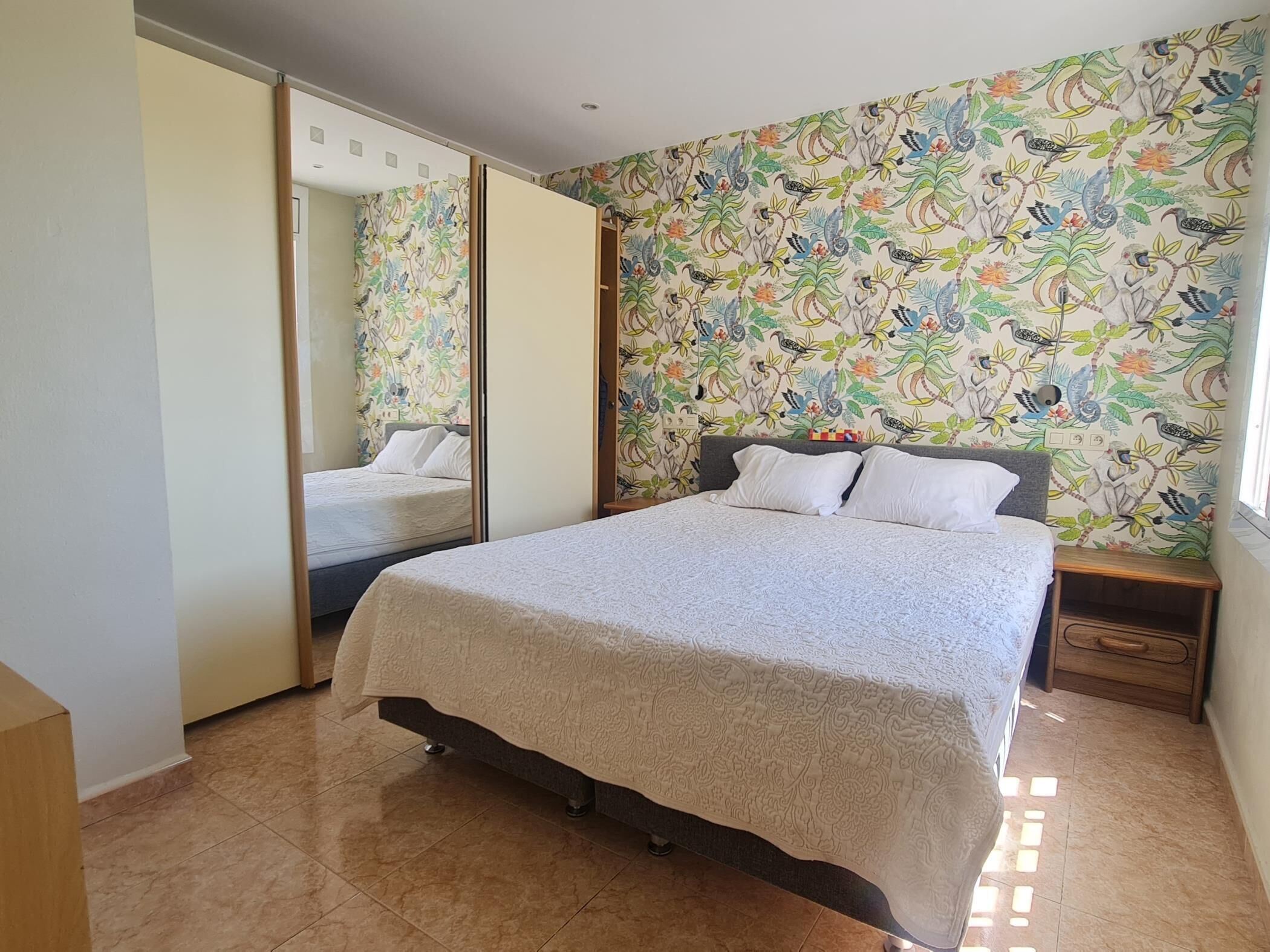 Une chambre à coucher avec un lit, une table de chevet, un miroir et un papier peint à motifs floraux.