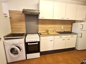 Une cuisine de taille réduite, équipée d’un lave-linge, d’une cuisinière, d’un évier et de meubles de rangement blancs.