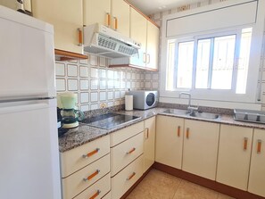 Une cuisine avec des meubles blancs, un four à micro-ondes, une machine à café et une fenêtre avec des stores.