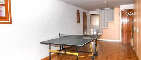 A room with a ping pong table, a wooden floor, a door, and a light fixture.