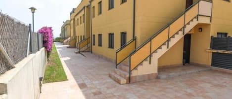 A building with a yellow facade, a staircase, and a paved walkway.