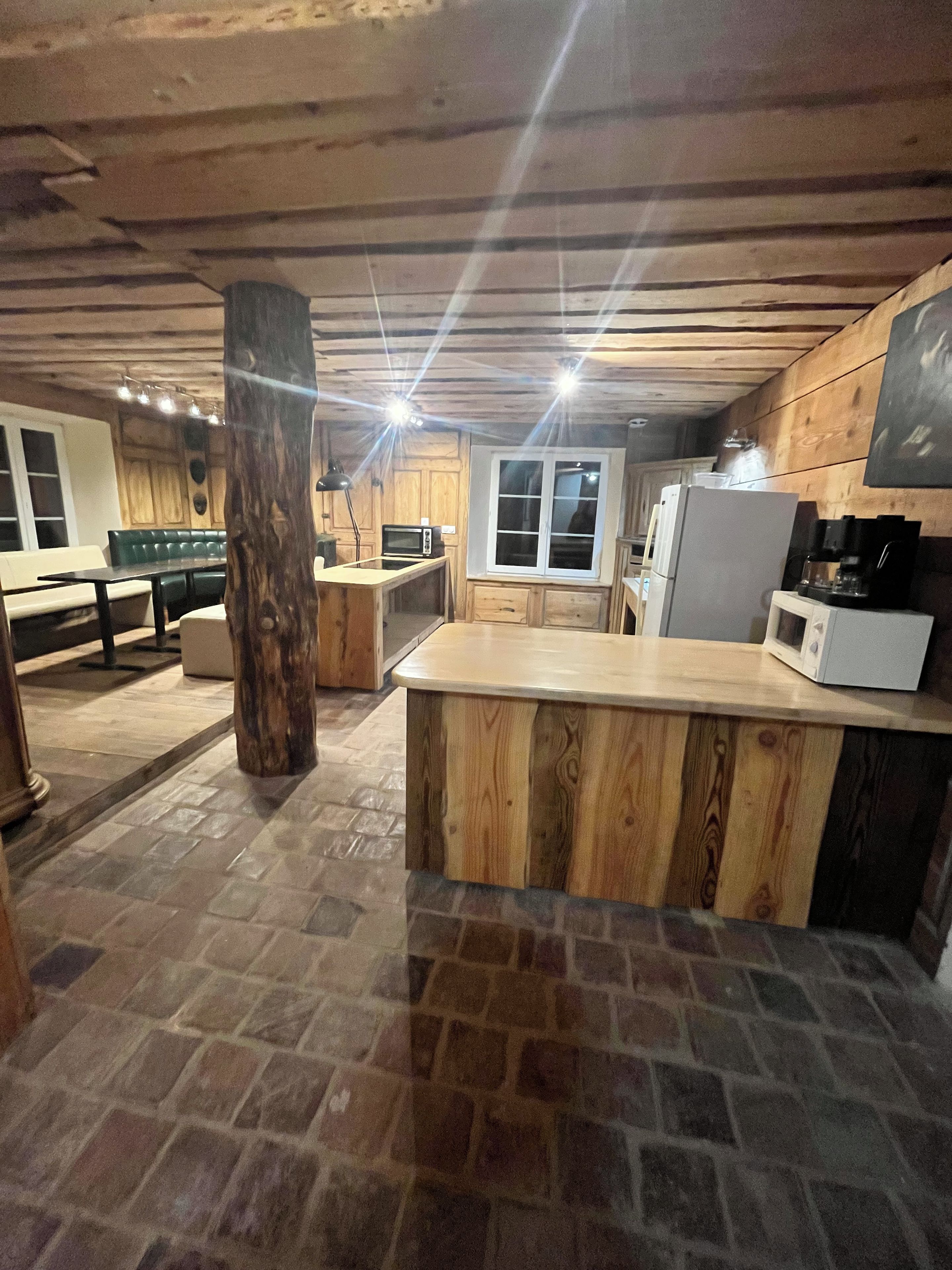 A kitchen with a stone floor, wooden cabinets, a central island, and a dining area with a bench.