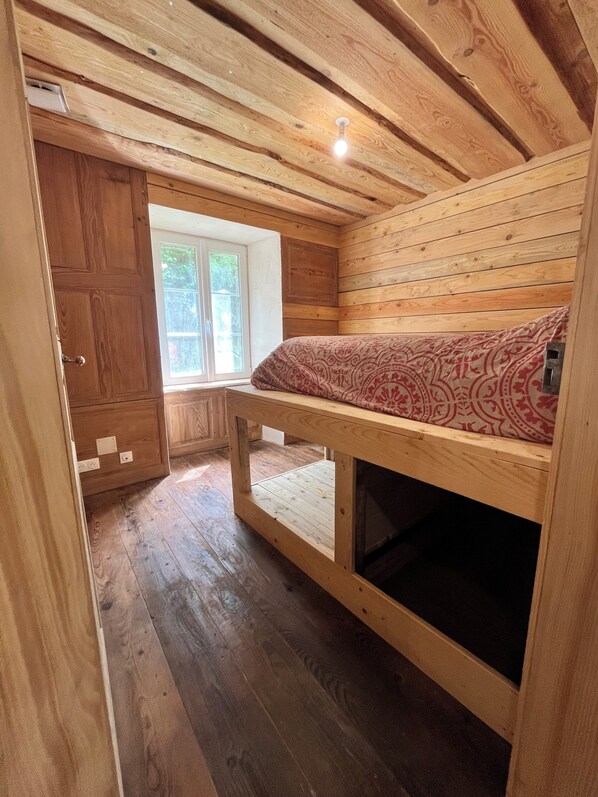 Une cabane en bois avec un lit superposé, une fenêtre et une porte.