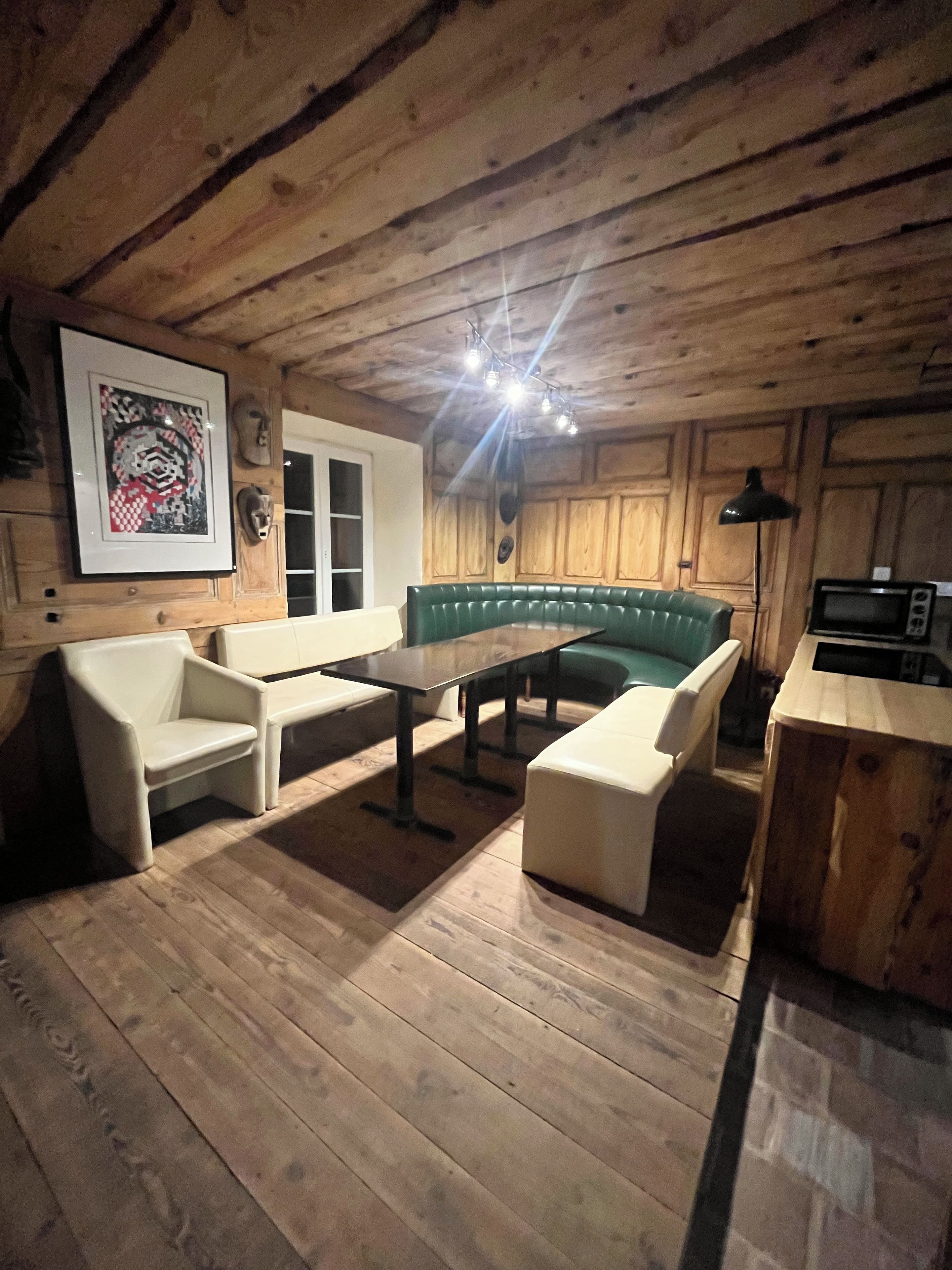 Un intérieur en bois comprenant une table à manger, des chaises, un canapé, un coin cuisine et une œuvre d’art encadrée accrochée au mur.
