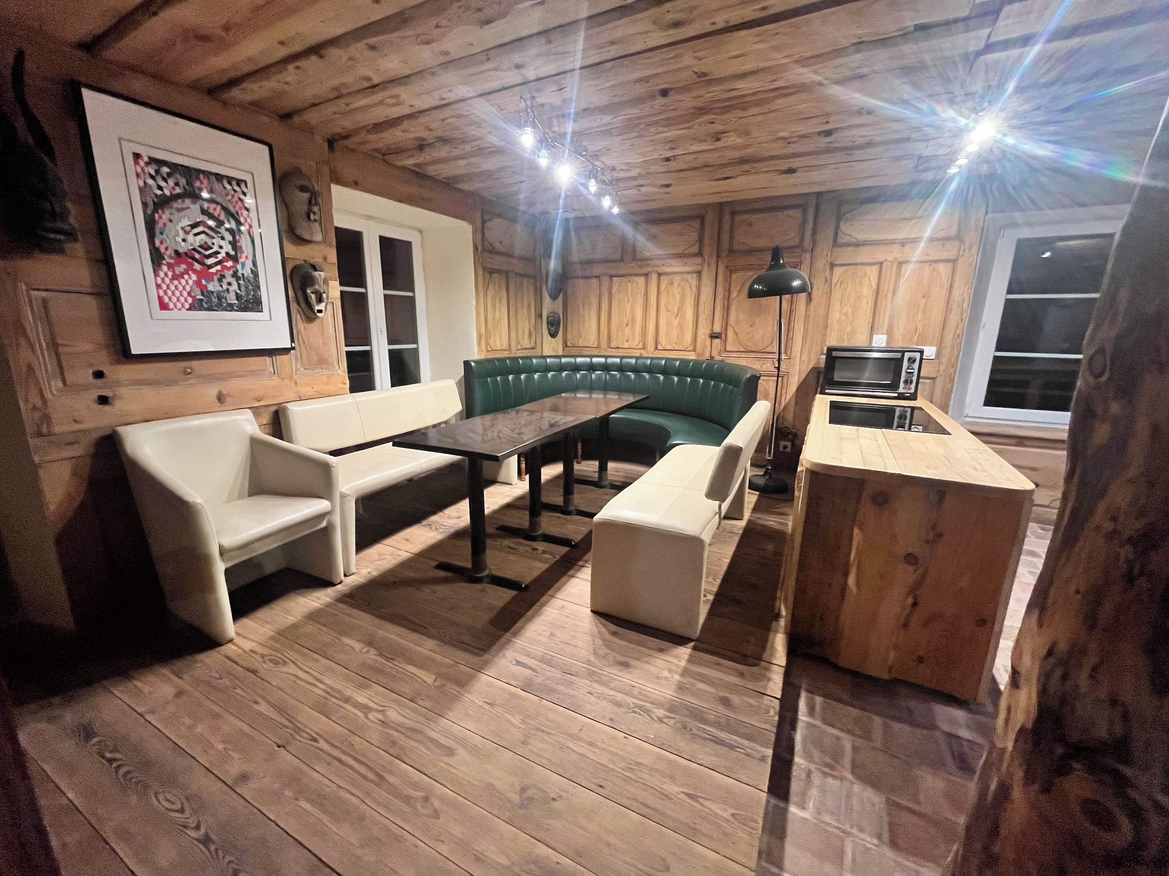 Un interior de madera con un sofá verde, sillones blancos, una mesa y una pequeña cocina.
