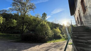 Un camino rural con banquina de grava, árboles y un edificio de fachada de piedra.