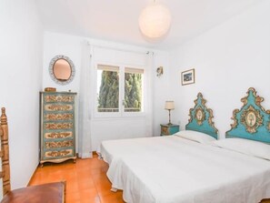Een slaapkamer met een bed, een dressoir, een raam en een lamp.