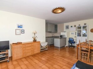 Een woonkamer met een televisie, houten meubels, een keukenhoek en een eettafel.