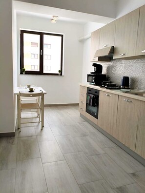 A modern kitchen with wooden cabinets, a built-in oven, and a window with a view of buildings. - Cozy 1-bedroom apartment in Bucharest with AC, 2.5 min to Mihai Bravu metro (București)
