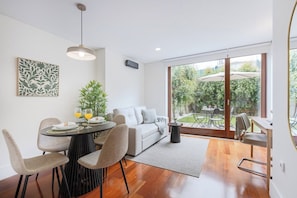 A modern living room with a dining area, a sofa, and a view of the garden through large windows. - 1BR With Private Patio Porto Urban Flats (Porto)