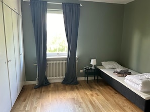A bedroom with a single bed, a nightstand, a lamp, and a window with curtains.