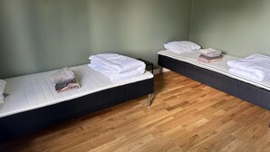 To senge med hvide sengetæpper, et lille bord med håndklæder og trægulv i et rum med grønne vægge.