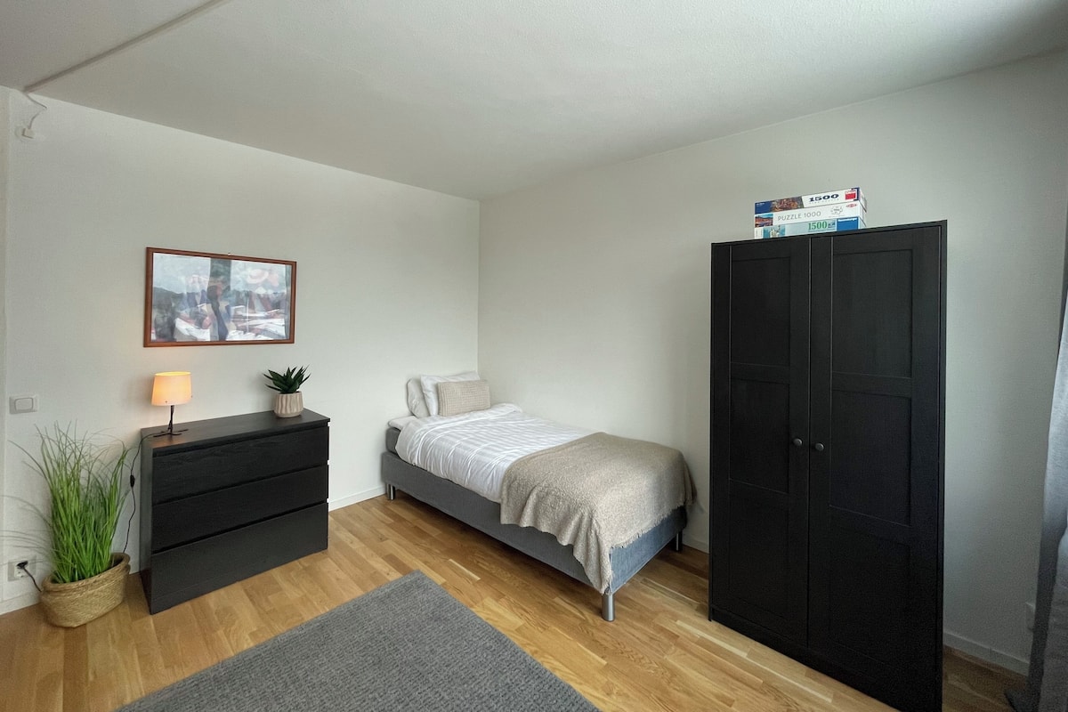 A bedroom with a bed, a dresser, a wardrobe, a lamp, a plant, and a framed picture on the wall.