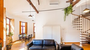 Amplia sala de estar con sofá de cuero negro, vigas de madera, una escalera y comedor con muebles de madera.