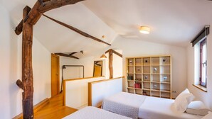 Una habitación con dos camas, vigas de madera, una estantería y una ventana.