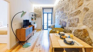 Une pièce avec un mur en pierre, une table à manger en bois mise avec des assiettes et des verres, un canapé et un téléviseur posé sur un meuble en bois.