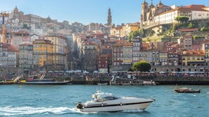 Un paysage urbain au bord de l’eau, avec des bâtiments historiques, une église imposante et un port animé où de nombreux bateaux sont amarrés.