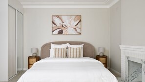 Ein Schlafzimmer mit einem großen Bett, zwei Nachttischen, einem Kamin und einem an der Wand befestigten Kunstwerk.