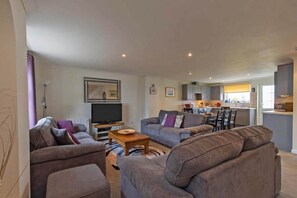 A living room with a sofa set, a coffee table, a TV, and a kitchen in the background. - Newquay - Atlantic Lodge - 10 - Pets - Pools - Gym (Newquay)
