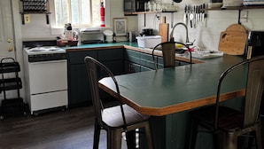 Una cocina con una isla central, taburetes de bar, estufa y diferentes utensilios de cocina.