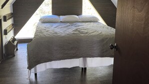 Un dormitorio con techo inclinado, una cama con ropa de cama blanca y un cuadro en la pared.