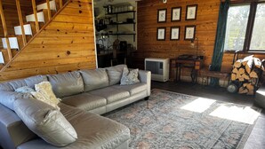 Una sala de estar acogedora con un sofá modular, un tapete estampado, paredes de madera, una escalera y una cocina visible a través de una puerta abierta.