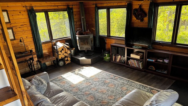 Un interior de cabaña acogedor con un sofá grande, una chimenea, un televisor y una estantería.