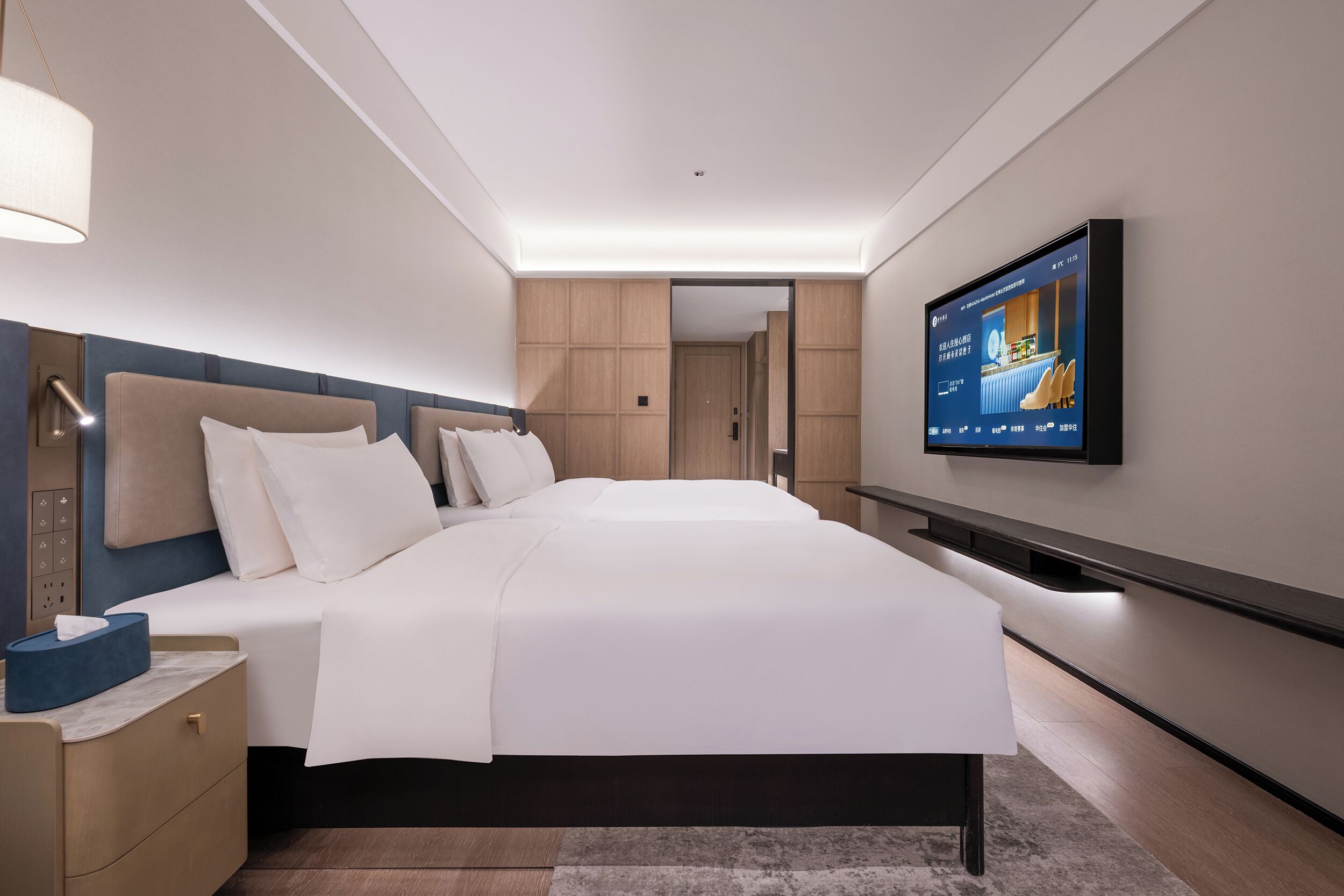 Una habitación de hotel moderna con una cama grande, un televisor en la pared y una mesita de noche con una lámpara.
