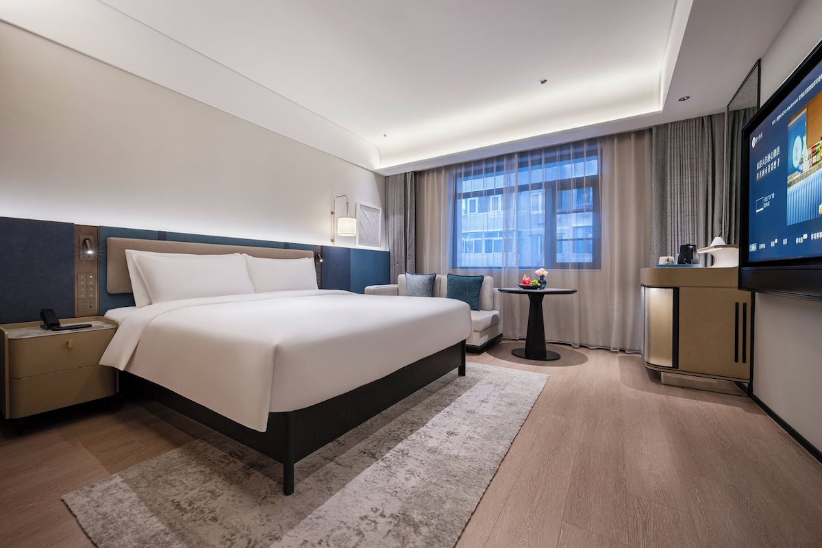 Une chambre d’hôtel moderne dotée d’un grand lit, d’un bureau, d’une télévision et offrant une vue sur la ville.