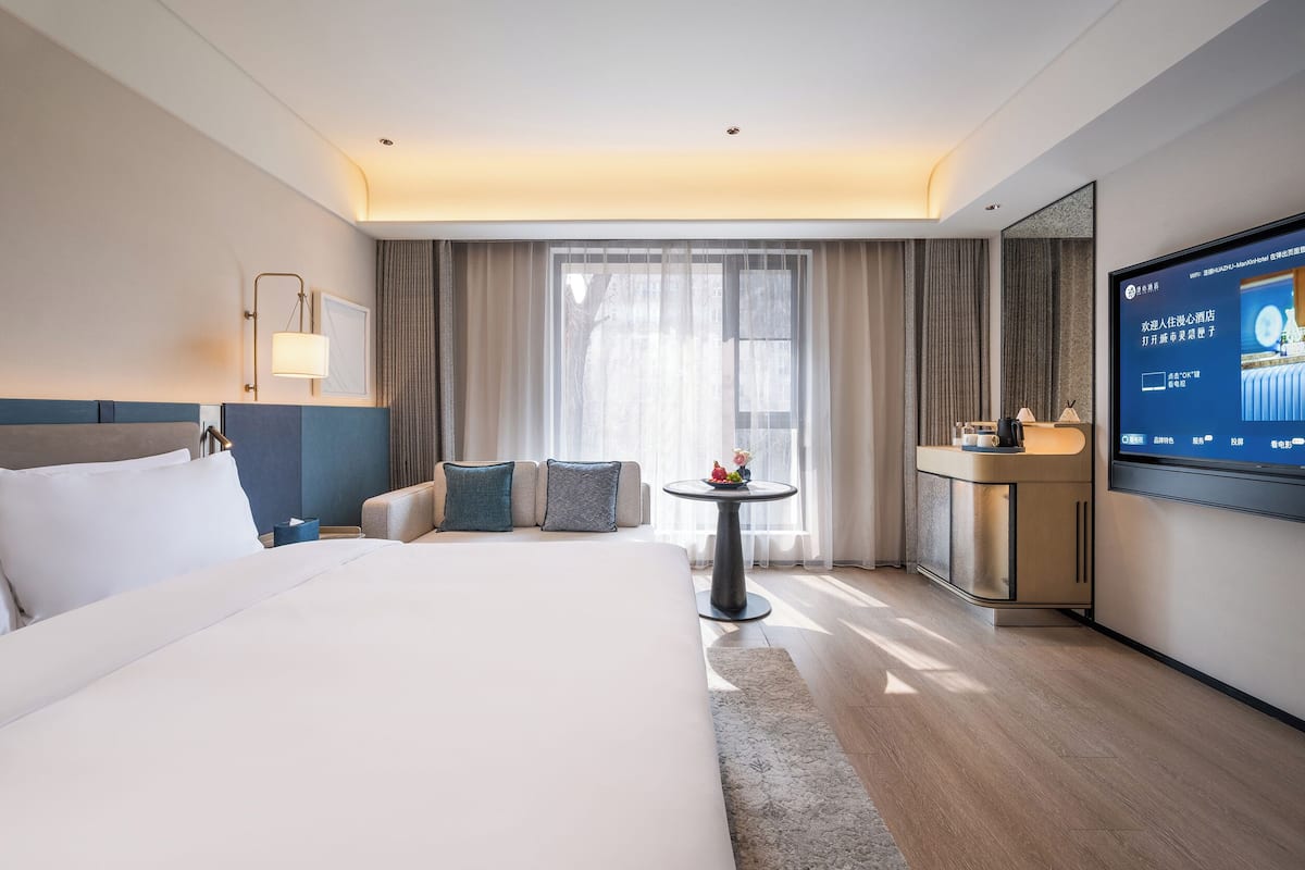 Une chambre d’hôtel avec un grand lit, une petite table ronde, une télévision et un bureau avec une lampe.