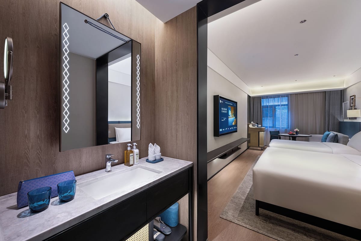 Une chambre d’hôtel moderne dotée d’un grand lit, d’une salle de bain avec un miroir, un lavabo et des articles de toilette, d’un téléviseur à écran plat et d’un bureau avec une chaise.