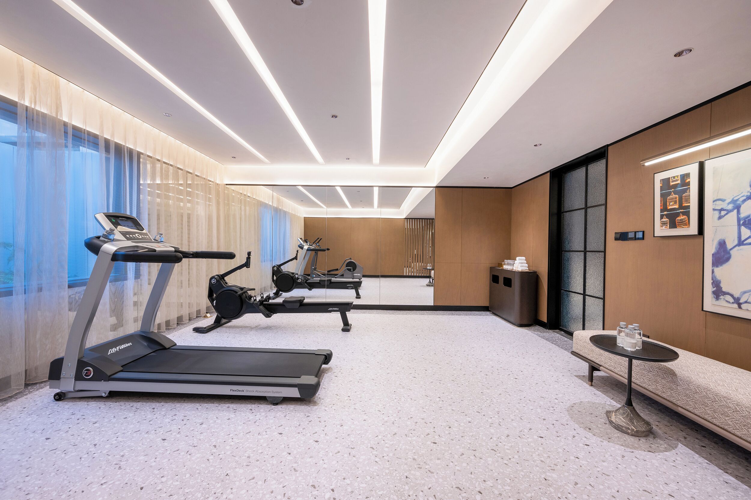 A modern hotel gym with treadmills, a rowing machine, and a bench.