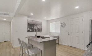A modern kitchen with a central island, white walls, and a large window with blinds. - 2-bedroom townhome in beautiful Tucson! (Tucson)