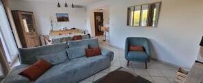 A living room with a sofa, a chair, a dining table, and a mirror on the wall. - A quiet home with a superb view of the historic village and a pool (VEZENOBRES)