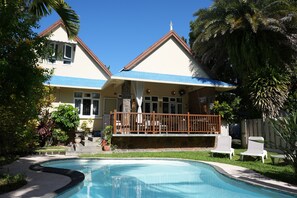 Ein zweistöckiges Haus mit Pool, einem Balkon mit Geländer und einem Garten mit verschiedenen Pflanzen.