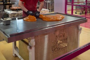 A person preparing food on a flat cooking surface with a metal container and a wooden table with engraved text.