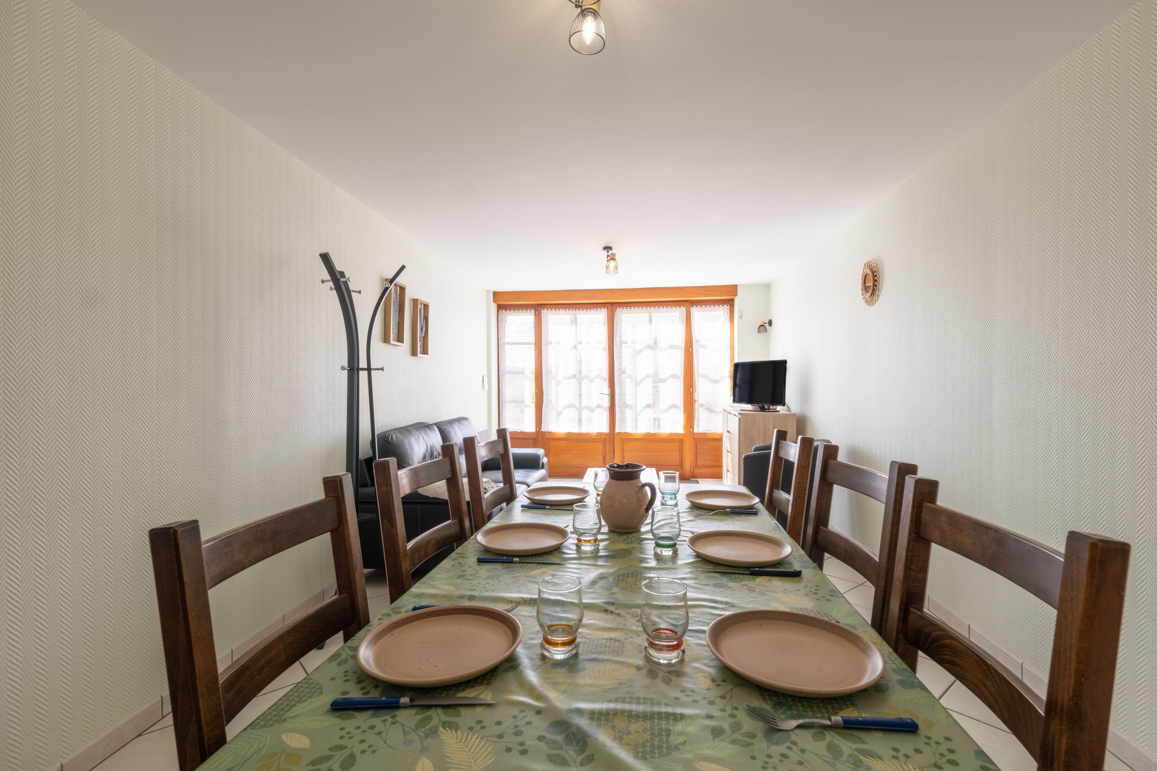 A dining area with a long table set for six, flanked by wooden chairs.