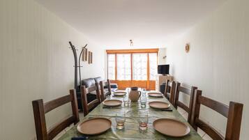 A dining area with a long table set for six, flanked by wooden chairs.