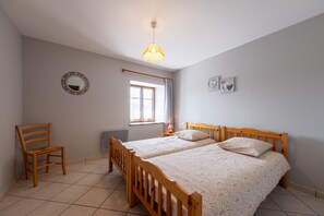 A bedroom with a wooden bed, a chair, a window with curtains, and a wall-mounted mirror.